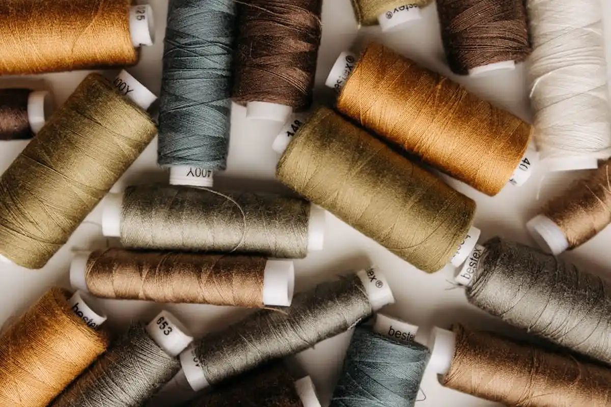 Close-up of assorted sewing thread spools in neutral and earthy tones on a light surface.