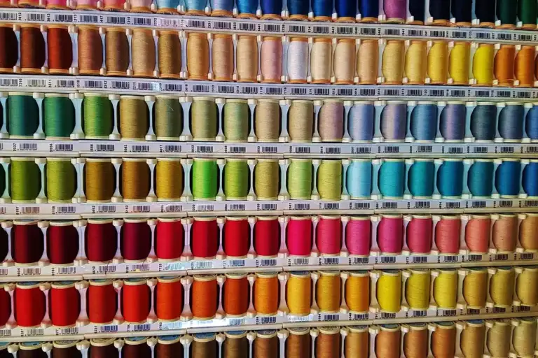 Rows of colorful thread spools arranged by color in a sewing shop, forming a rainbow display.