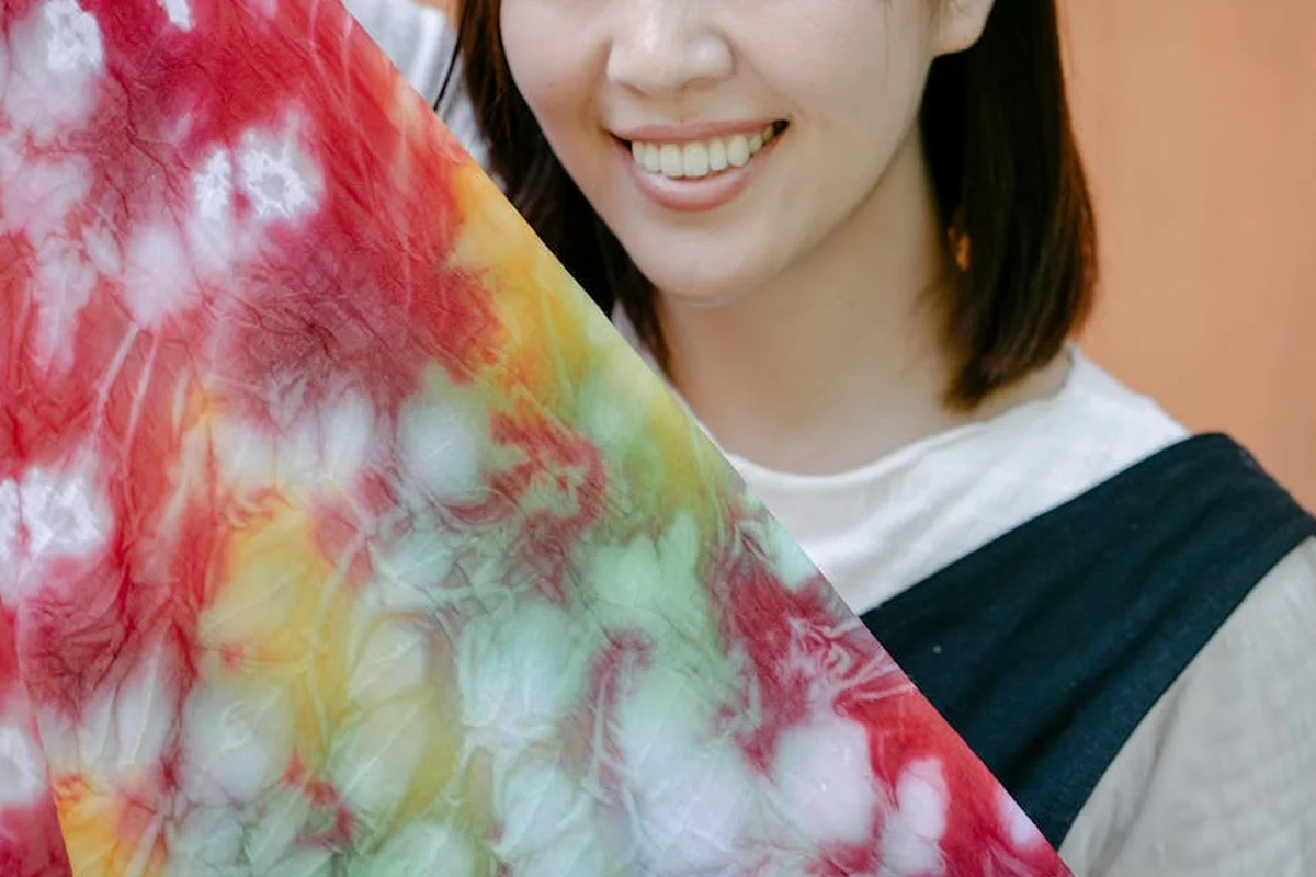 Smiling person holding a multicolored tie-dyed fabric