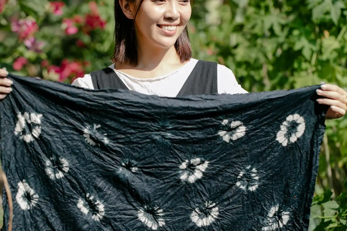 Smiling person outdoors holding up a black fabric with white circular tie-dye patterns.