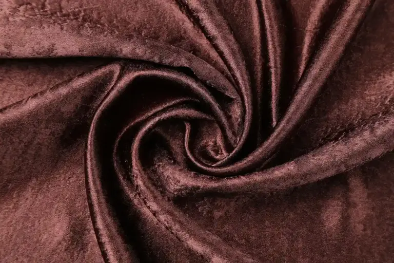 Close-up of burgundy velvet fabric twisted into a spiral, highlighting soft pile and texture.