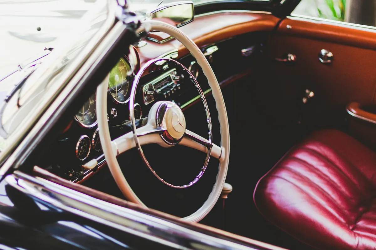 Interior of a vintage car featuring a cream steering wheel and red leather seats, highlighting the aged leather patina.