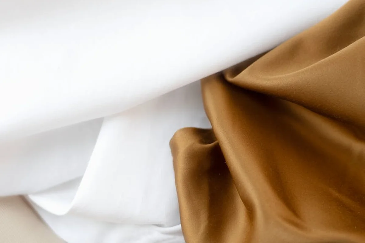 Close-up of white and bronze satin-like viscose/rayon fabrics with soft folds to illustrate wrinkles.