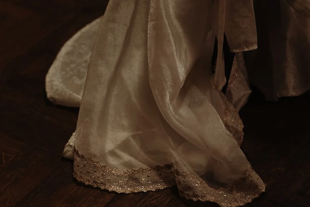 Close-up of a silky viscose fabric with decorative lace trim draped over a dark wooden floor.