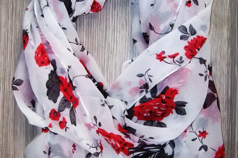 Light floral scarf made of viscose fabric with red and pink flowers on a pale background, showing soft drape and smooth sheen.