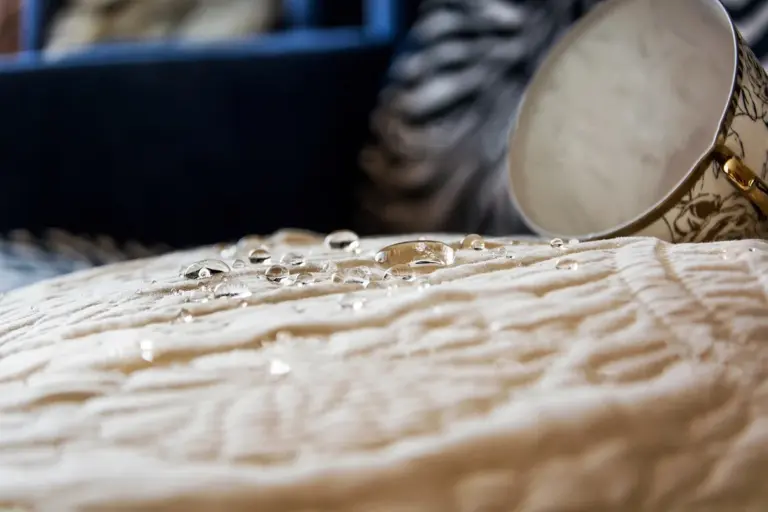 Close-up of water droplets beading on a beige fabric with a tilted cup in the background.