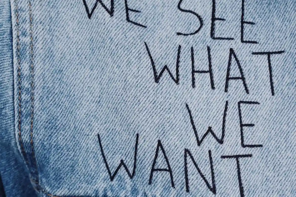 Close-up of blue denim fabric with handwritten text reading 'WE SEE WHAT WE WANT'.