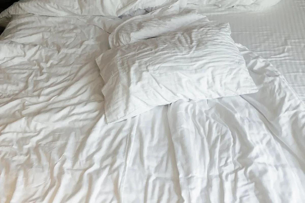 Close-up of white wrinkled bed sheets with two pillows, showing the texture of bedding fabrics
