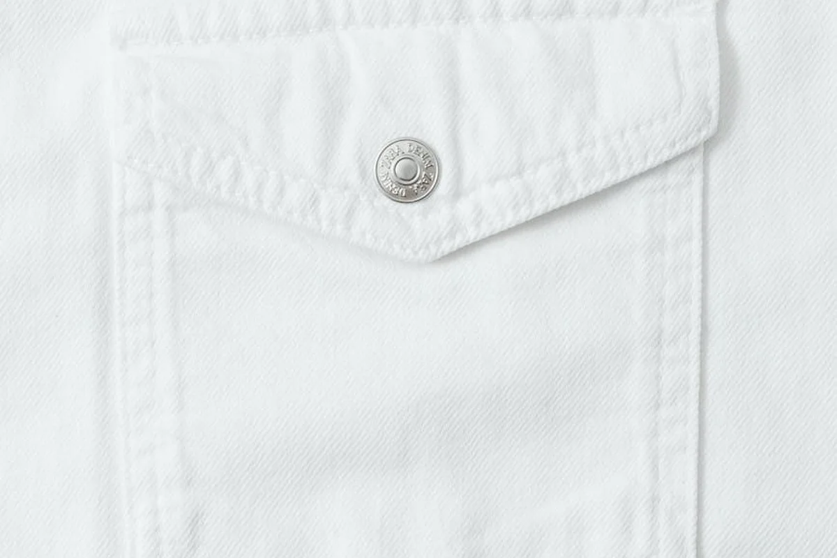 Close-up of white cotton fabric with a front pocket and metal button