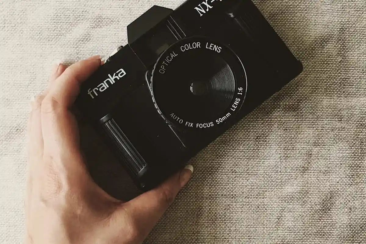 A hand holding a black vintage camera resting on beige textured linen fabric.