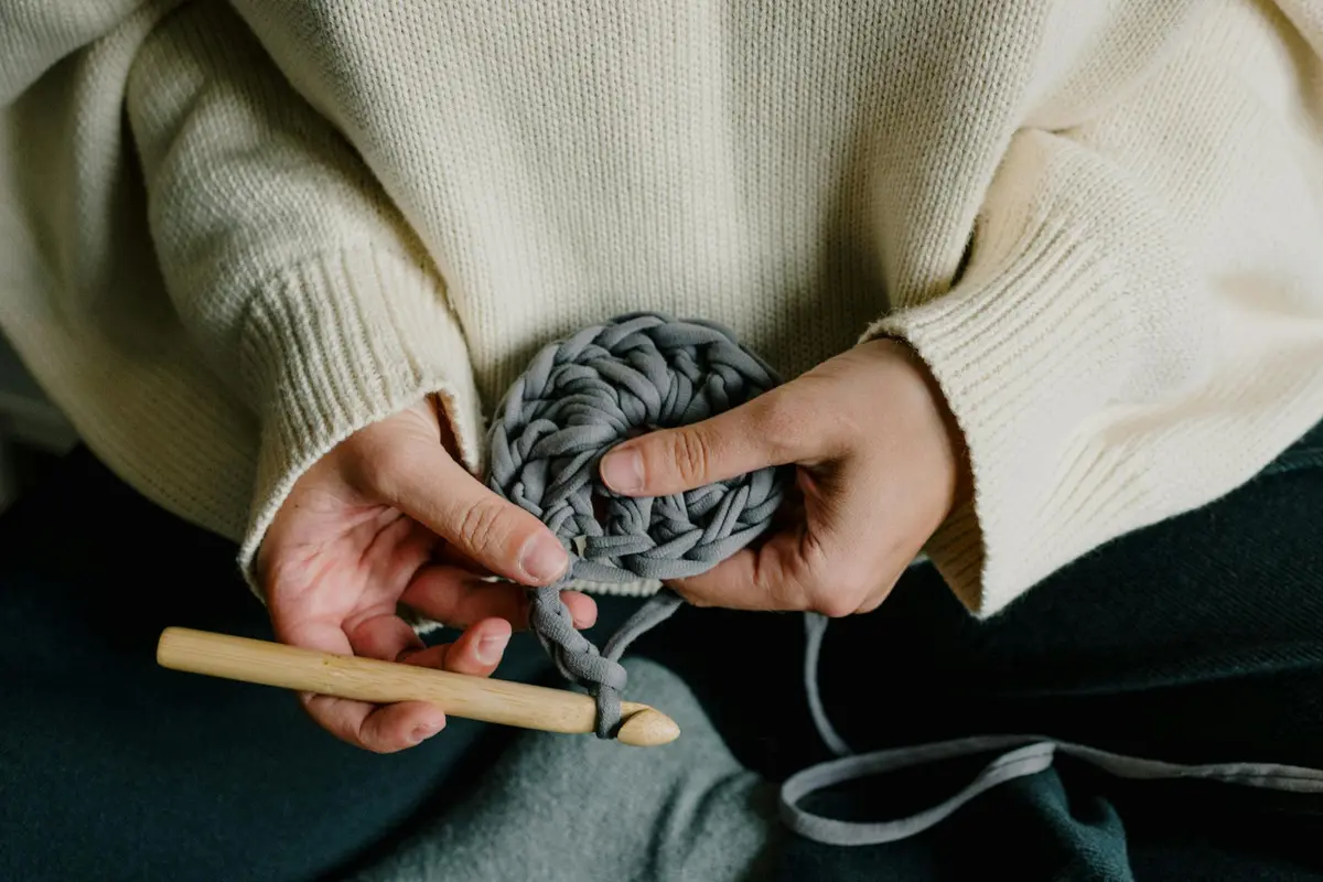 Close-up of hands knitting thick gray wool using a wooden knitting needle