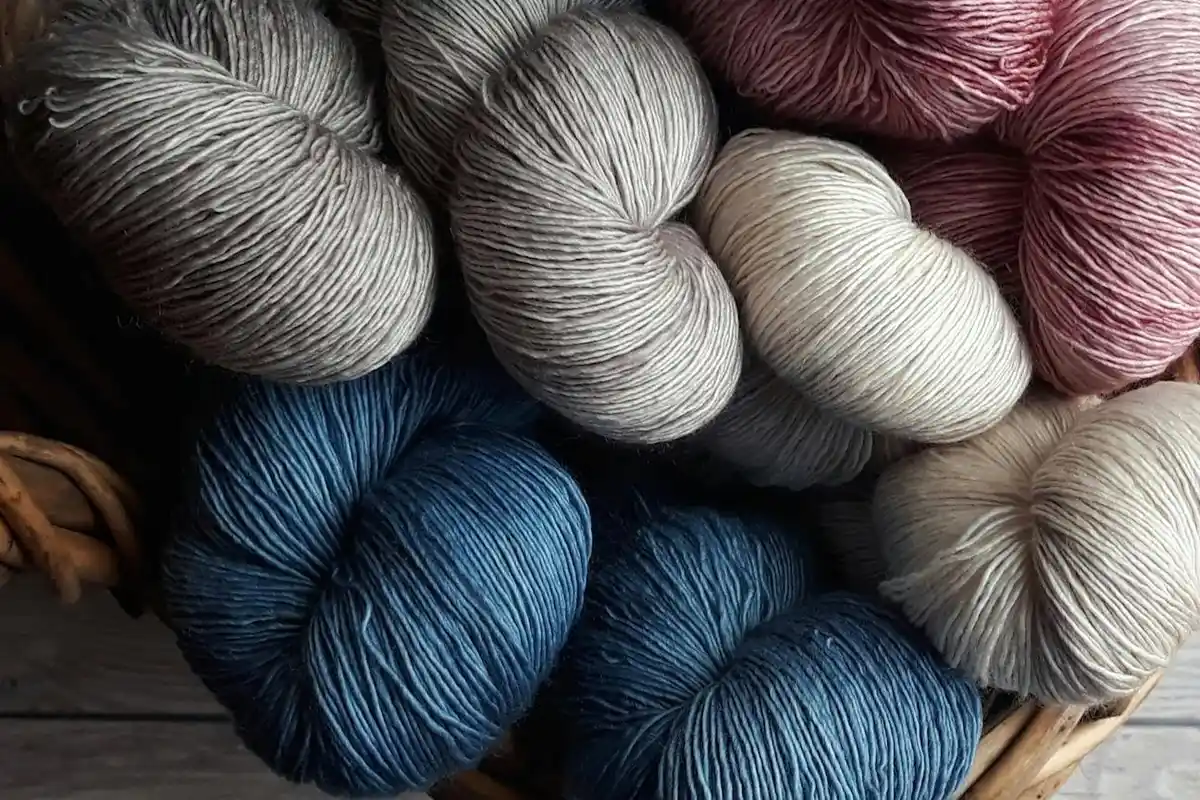 Assorted skeins of yarn in a basket in shades of blue, gray, white, and burgundy