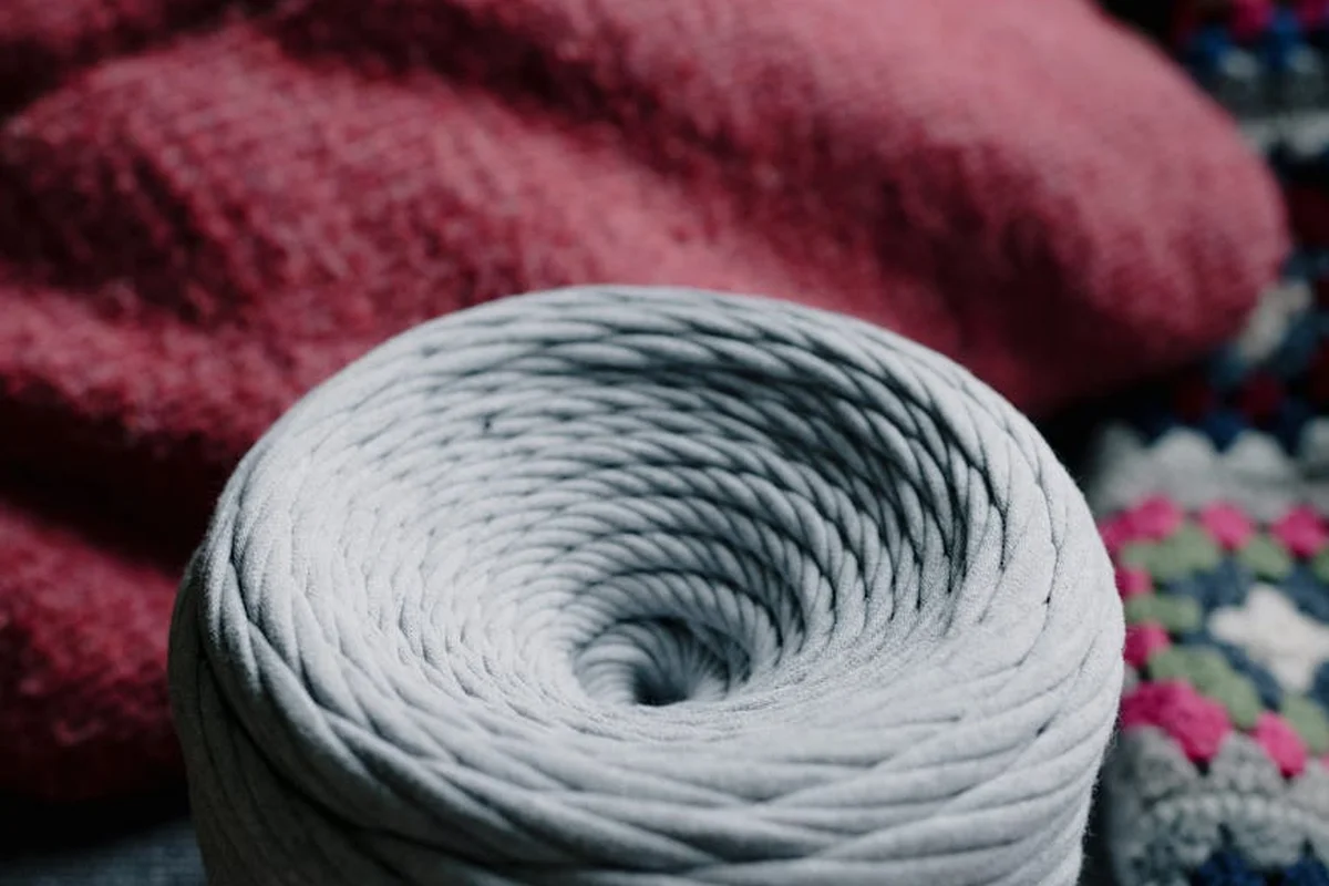 Close-up of a coiled gray yarn skein with a pink fabric background.