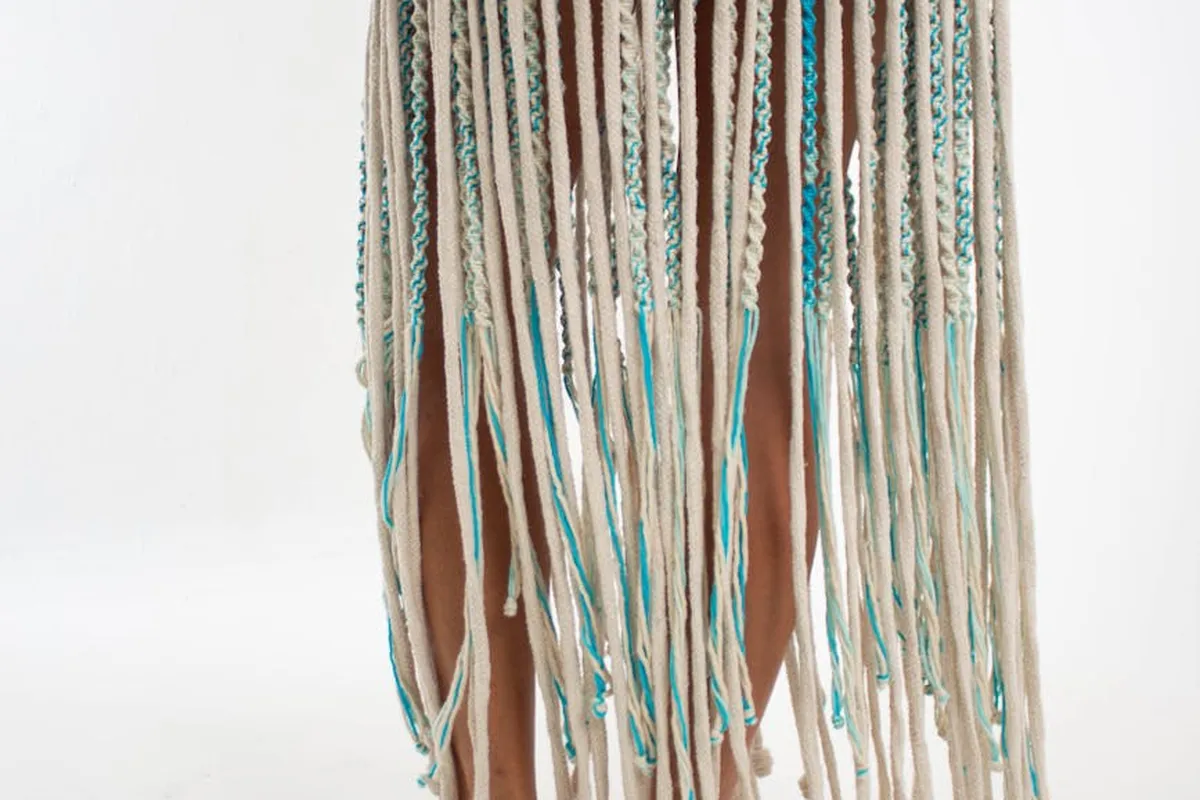 Multiple yarn strands in teal, cream, and brown hanging down in front of a light background.