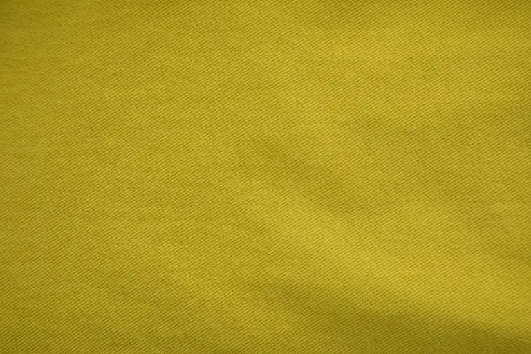 Close-up of mustard-yellow knit fabric showing a fine diagonal weave texture