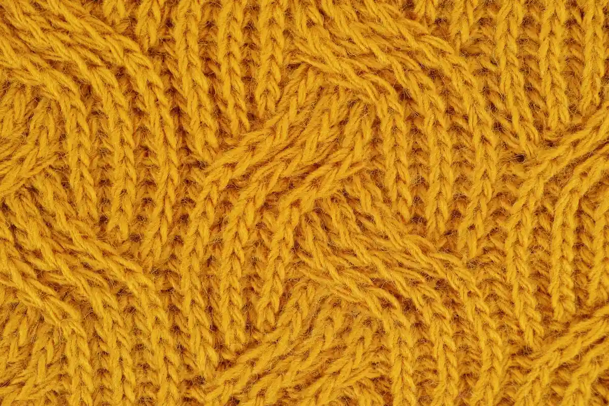 Close-up of mustard-yellow knitted wool fabric showing textured stitches